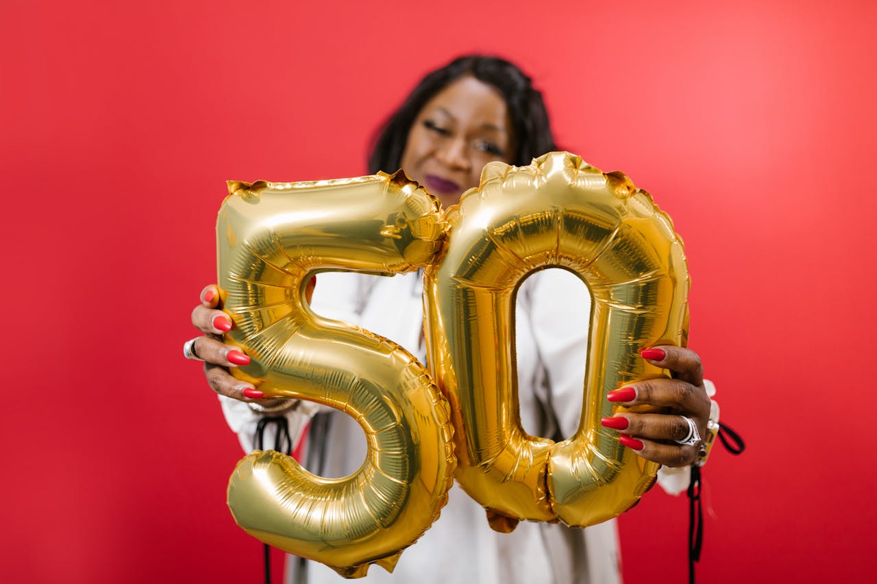 Crafting Captivating Headlines: Your awesome post title goes here Woman holding gold number 50 balloons on a vibrant red background, symbolizing celebration.