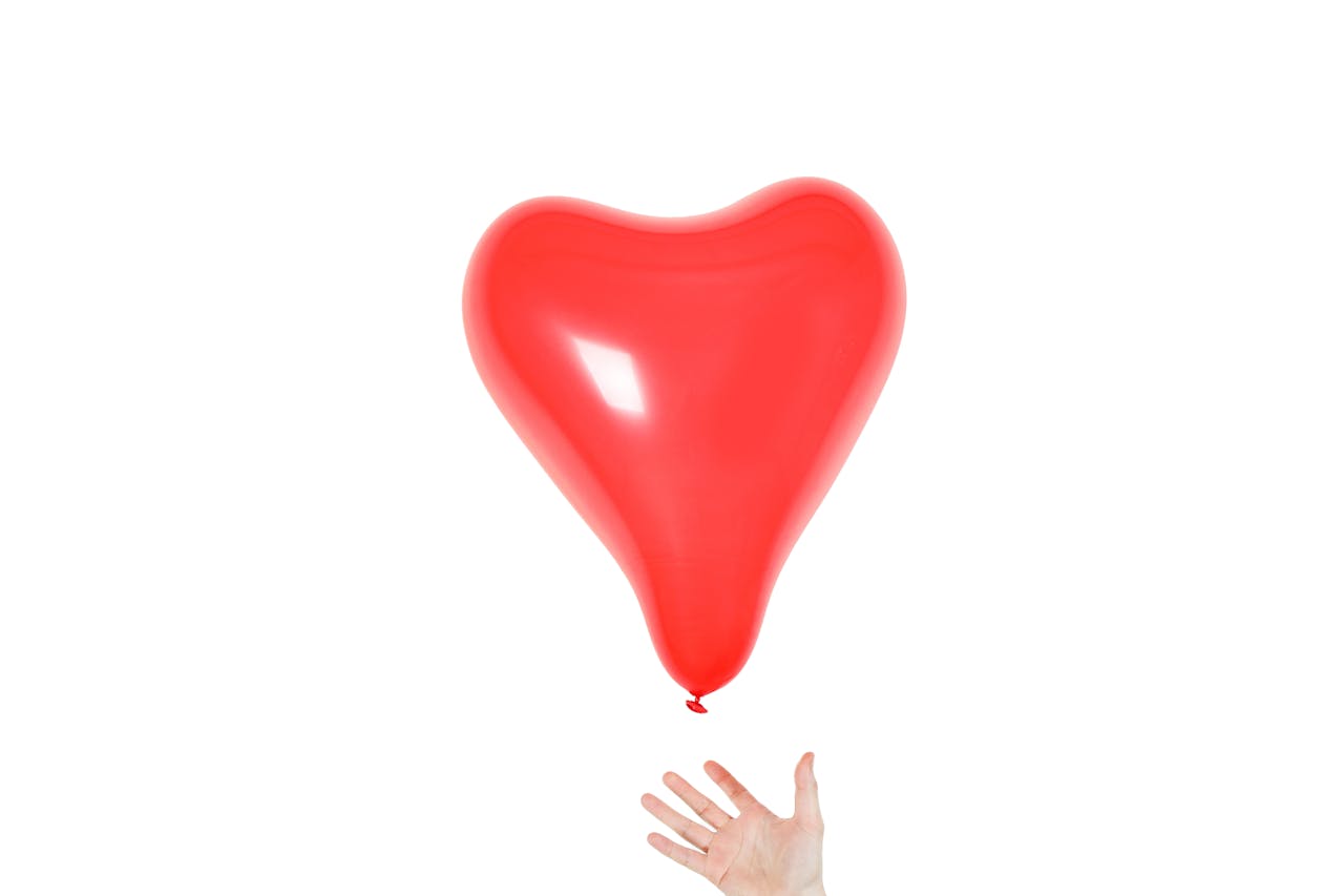 project-01-a A vibrant red heart-shaped balloon floating with a hand reaching for it on a white background.